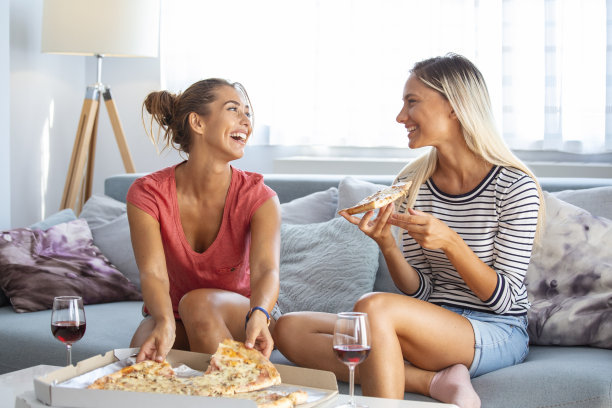 两个女性朋友一边喝着红酒，吃着披萨，一边八卦，一边用手机在她的朋友的社交网络上展示照片图片下载