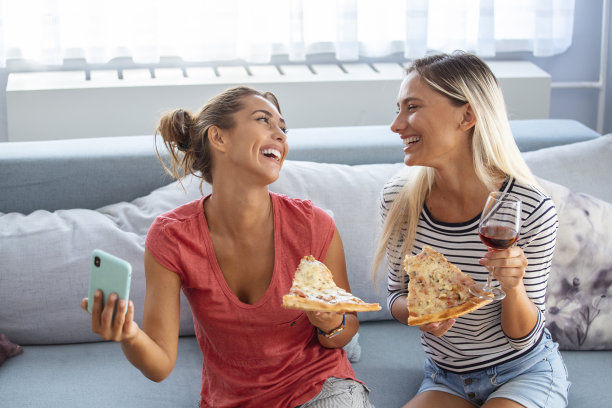 朋友们吃着披萨，微笑着自拍。他们分享披萨，用智能手机自拍。图片下载