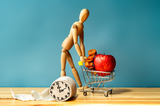 木头人推着一辆装满水果的购物车，旁边是一卷卫生纸。消化问题的概念。图片下载