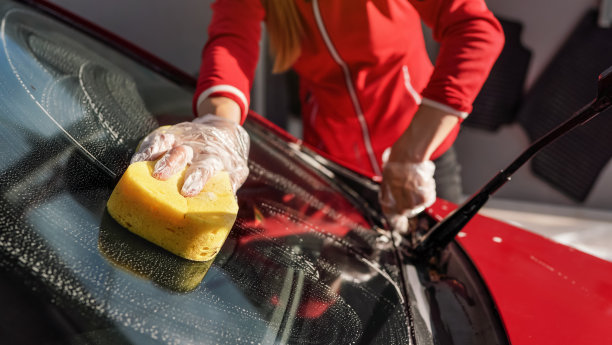 年轻女子清洁她的汽车挡风玻璃，特写细节手戴手套拿黄色海绵图片下载