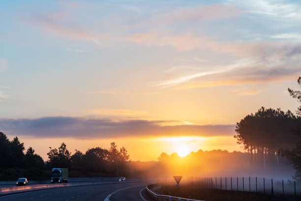 公路的风景在黎明，太阳开始升起，雾在树之间。图片下载