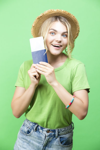 旅行的概念。迷人的可爱微笑的年轻女孩的肖像在草帽持有护照与票孤立在时尚的绿色背景图片下载