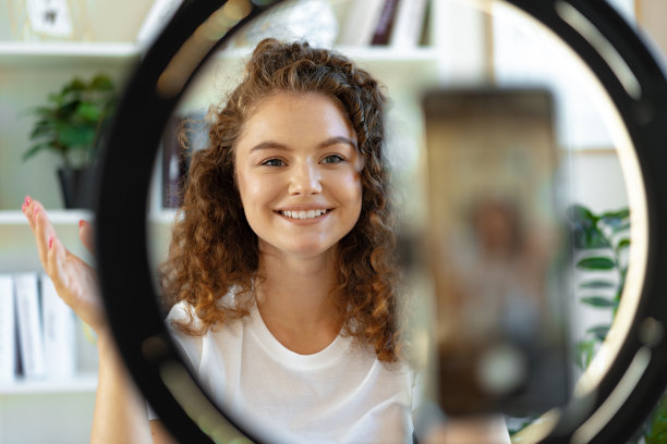 年轻的卷发女博主在家里的桌子上录制视频图片下载