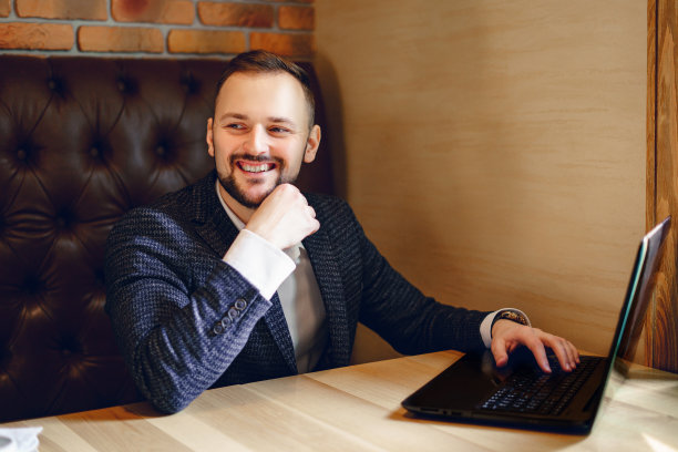 在餐馆或咖啡馆的桌子旁，一个穿着西装、拿着笔记本电脑的年轻人图片下载