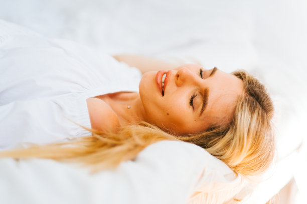 迷人的白种人幸福的肖像与金发的女人，躺在床上的白色毯子在阳光明媚的日子。图片下载