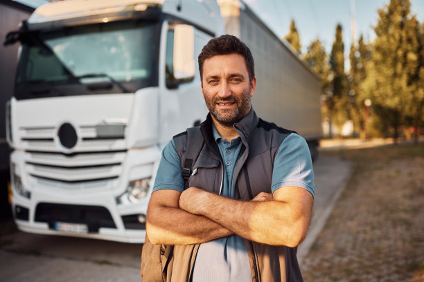 快乐的司机双手交叉站在卡车停车场，看着镜头。图片下载