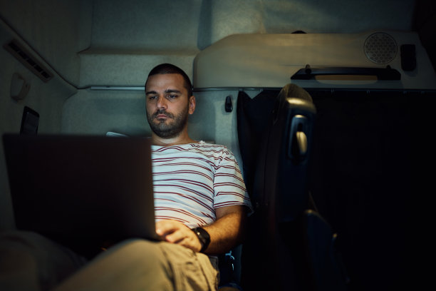年轻的卡车司机晚上在小木屋休息时使用笔记本电脑。图片下载