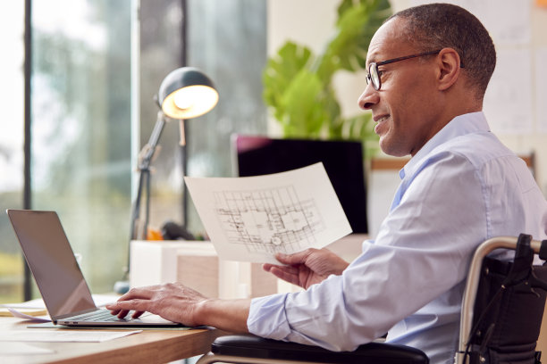 坐在轮椅上的成熟男性建筑师在办公室办公桌前研究新建筑的计划图片下载