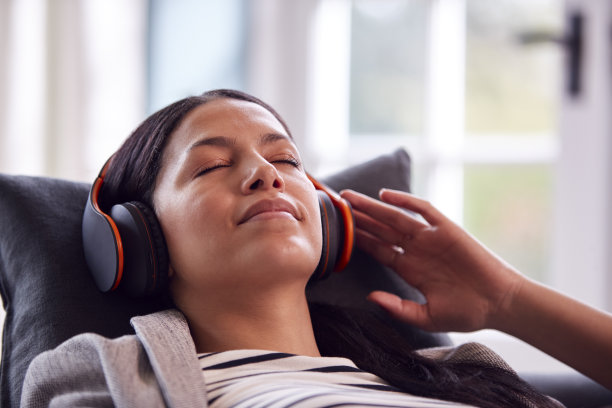 女子戴着无线耳机躺在沙发上听音乐放松休息图片下载