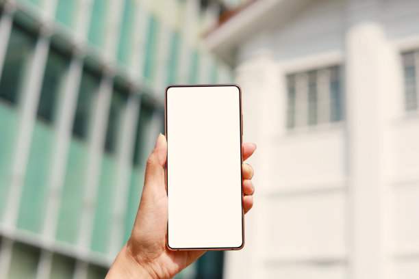 照片中，一名女子手拿着一部带有建筑背景的白屏智能手机图片下载