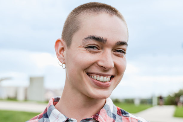 肖像的年轻秃顶妇女微笑的相机户外在公园城市-焦点的脸图片下载