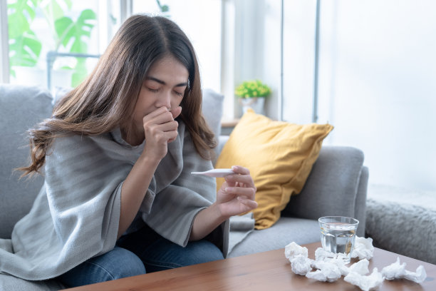患有流感的亚洲妇女坐在家里客厅的沙发上。图片下载