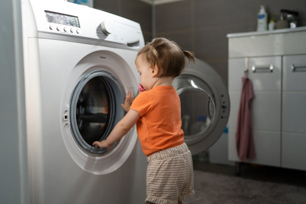 一个女孩小白种人学步的孩子女儿站在洗衣机旁，在厕所里开或关门检查和学习早期发展和成长的恶作剧拷贝空间的概念图片下载