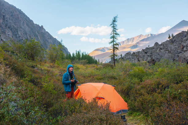 阳光明媚的日子里，游客带着相机在山谷郁郁葱葱的植被中靠近橙色帐篷。天气好的时候，人们会在秋天爬山时在大自然中休息。摄影师拍摄野生自然的照片。图片下载