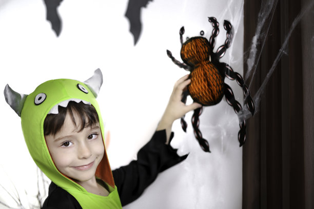 穿着怪物服装的快乐小男孩摸了摸蜘蛛网上的橙色纸蜘蛛。图片下载