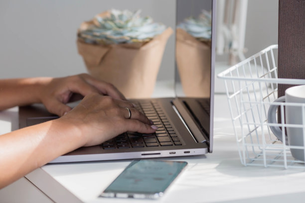 一个自由职业女性的手坐在家里的办公室里，拿着笔记本电脑和智能手机。女人在家工作。工作日的开始。人力资源管理与招聘的概念图片下载