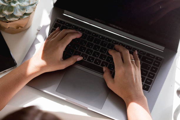 一个自由职业女性的手坐在家里的办公室里，拿着笔记本电脑和智能手机。女人在家工作。工作日的开始。人力资源管理与招聘的概念图片下载