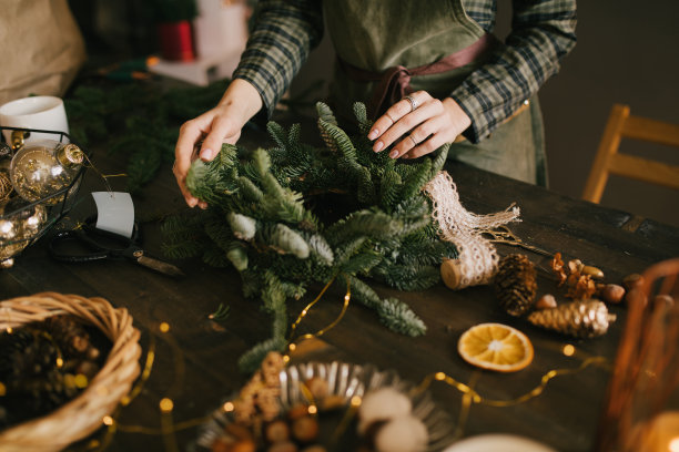 千禧一代的女性在作坊中用天然松枝和节日装饰品制作圣诞花环。图片下载