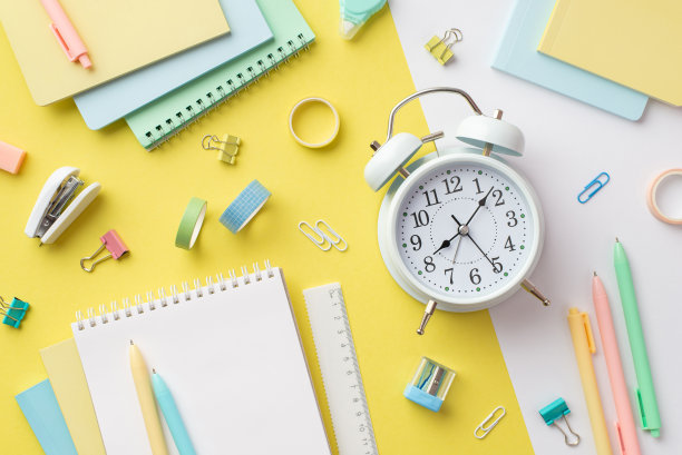 学校附件的概念。闹钟彩色记事本卷尺笔活页夹胶带和订书机在双色黄色和白色背景的俯视图照片图片下载