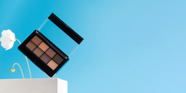 用于装饰化妆的眼影盘悬浮在蓝色背景上的白色底座上，上面有一朵花。横幅图片下载