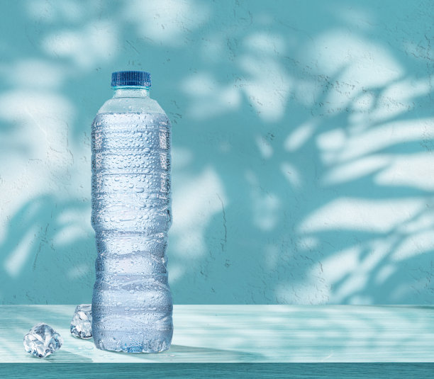 桌上放着一瓶装有冷凝液滴的冷冻水和两块冰块。蓝色背景。图片下载