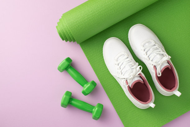 健身器材的概念。俯视图照片白色运动鞋在绿色运动垫和哑铃孤立粉彩紫色背景图片下载