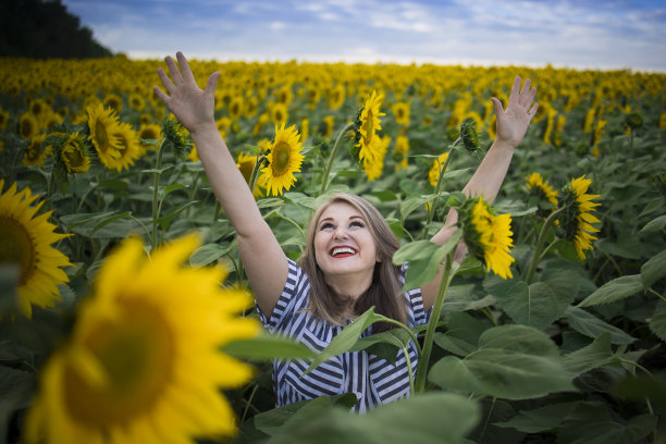快乐美丽的中年妇女高兴地享受向日葵田盛开的晴天图片下载