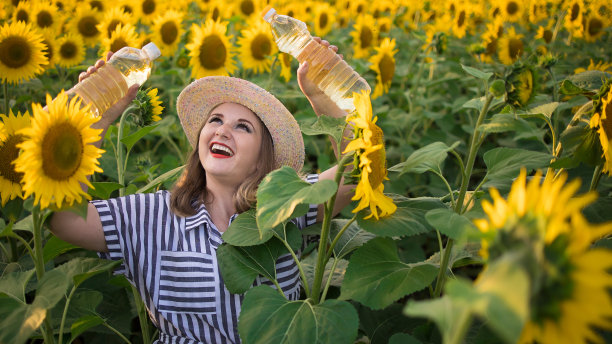美丽微笑的中年农妇手里拿着金色的葵花籽油，在阳光灿烂的向日葵田图片下载
