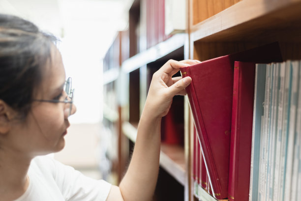 图书馆与教育理念，亚洲女性从图书馆书架上挑选书籍。图片下载