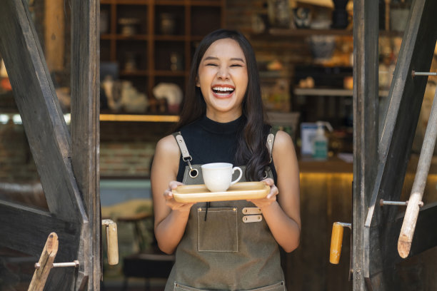亚洲幸福女人的肖像站在他的咖啡店面前，手端着目前的木托盘与咖啡小生意欢迎重新开业，亚洲女性微笑的咖啡师捧着咖啡图片下载