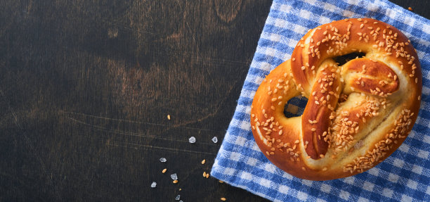 巴伐利亚椒盐脆饼和一杯啤酒。慕尼黑啤酒节的食物菜单，传统的盐椒盐脆饼在古老的深色木制背景上。带有文本空间的俯视图。啤酒节的主题图片下载
