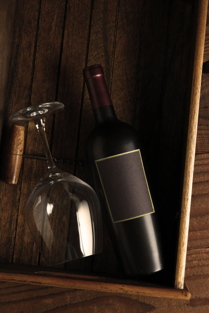 葡萄酒静物:扁平的酒瓶、酒杯和开瓶器放在一个有温暖侧灯的木箱里。带有拷贝空间的垂直格式。图片下载