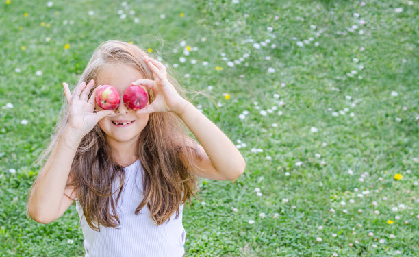 一个小女孩坐在草地上，手里拿着苹果，捂着眼睛。图片下载