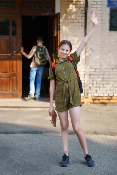 图为，一名十几岁的女学生站在学校门口，挥手致意图片下载