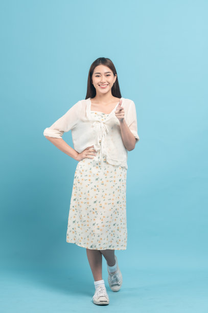 美丽的年轻亚洲女子在白色连衣裙与花卉图案孤立在蓝色的背景图片下载