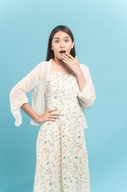 美丽的亚洲年轻女子在白色连衣裙与花卉图案的感觉惊喜孤立在蓝色的背景图片下载