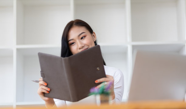 有吸引力的美丽的亚洲女人在读一本书在家庭办公室。图片下载