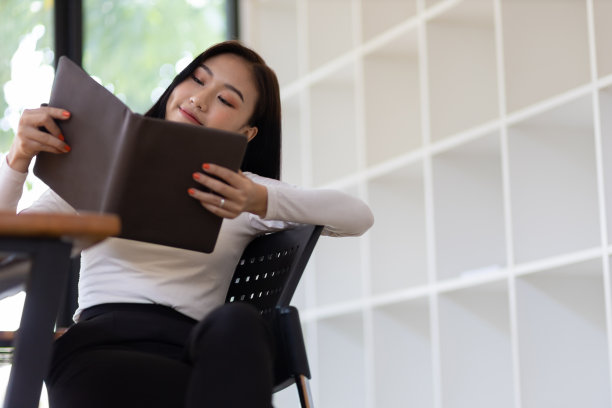 有吸引力的美丽的亚洲女人读一本书，写在记事本在家里的办公室。图片下载