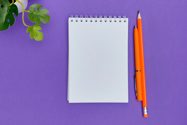 从以上观点。橙色的钢笔，铅笔，绿色的植物。紫色的背景。图片下载