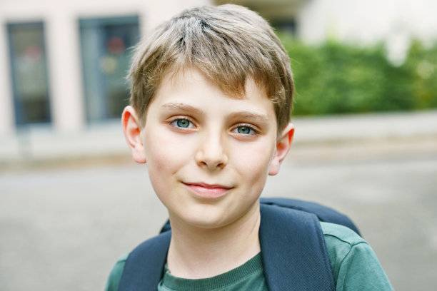 快乐的小男孩带着背包或挎包。在温暖阳光明媚的夏天，小学生在去小学或中学的路上。健康的孩子在城市的大街上。图片下载