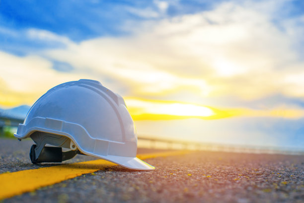 白色安全帽放置在道路黄色实线上的近景，以夕阳和蓝天为背景，日落时工地上的安全帽，安全与工程概念。图片下载