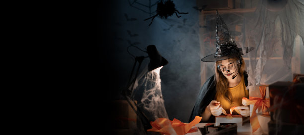 年轻的女人与万圣节化妆面具的企业主坐在家里的办公室系橙色蝴蝶结的盒子。图片下载