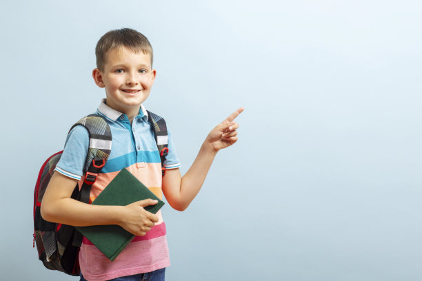 回到学校。快乐的小学生戴着眼镜拥抱着书本，指着蓝色背景上的一片空白。自由空间图片下载