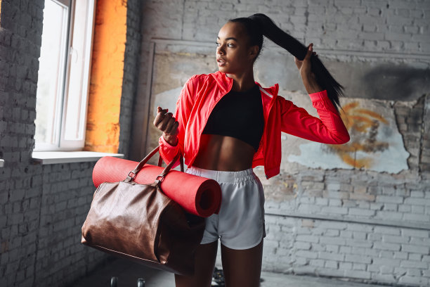 迷人的年轻女子在运动服装携带包与运动垫和调整头发图片下载