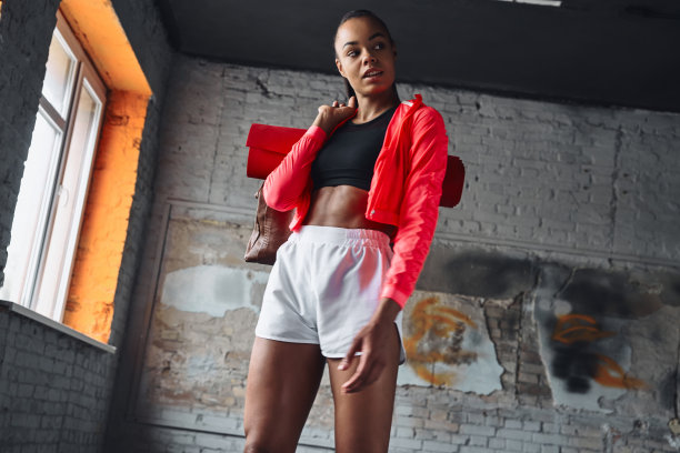 自信的年轻非洲妇女在运动服装携带包与运动垫和微笑图片下载