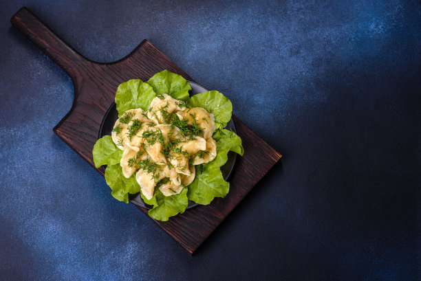 新鲜美味的土豆饺子，点缀着绿色蔬菜和生菜叶子在一个黑色的盘子里图片下载