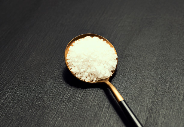 烹饪、香料、风味尽在一勺优雅高档的专业厨房设计，为精致的用餐之用。顶部的看法金和黑色勺子粗盐对一个黑暗的背景图片下载