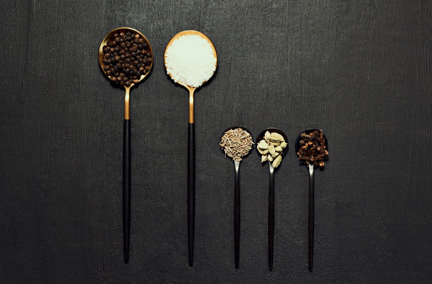 食物、烹饪和烘焙用香料、香草和调味料放在厨房上方的一张深色桌子上。盐，胡椒和小豆蔻的俯视图显示与平面和copyspace准备一顿饭图片下载