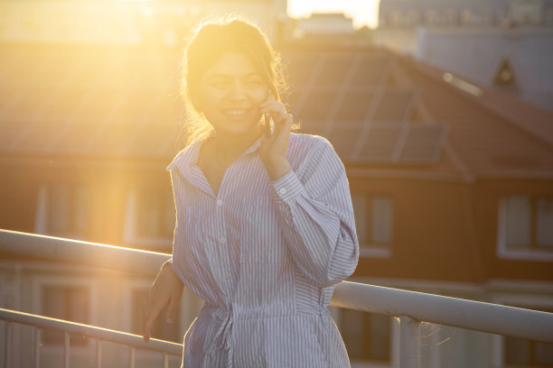 日落时分，一个年轻女子在阳台上打电话。图片下载
