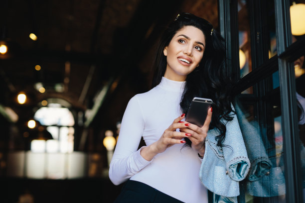 梦幻时尚的褐发美女，迷人的外表，穿着优雅，拿着手机，看着照片，回忆她生活中的愉快时刻。表情凝重的女人图片下载